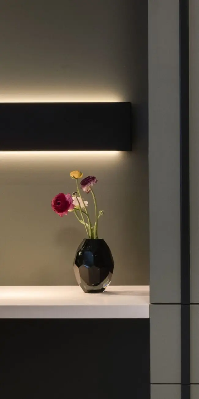 Schwarze Vase mit Ranunkeln unter indirekt beleuchtetem Wandboard, Haus der Standesbeamten Haus 3