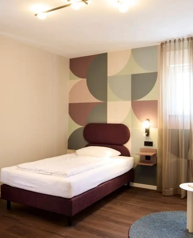 Helles Einzelzimmer mit Bett, Schreibtisch und rosa Sessel im Gästehaus 2, Haus der Standesbeamten