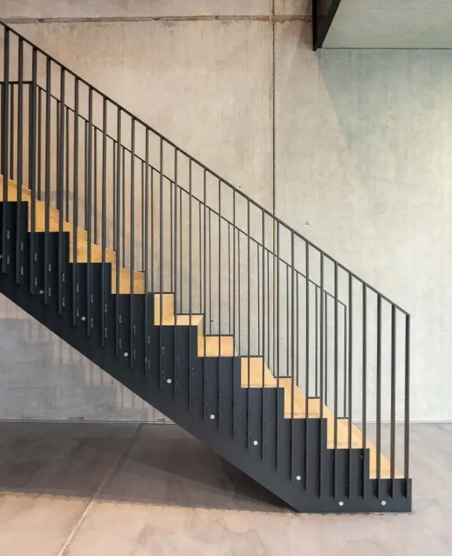 Schwarze Stahltreppe mit Holzstufen vor Sichtbetonwand bei Belfox