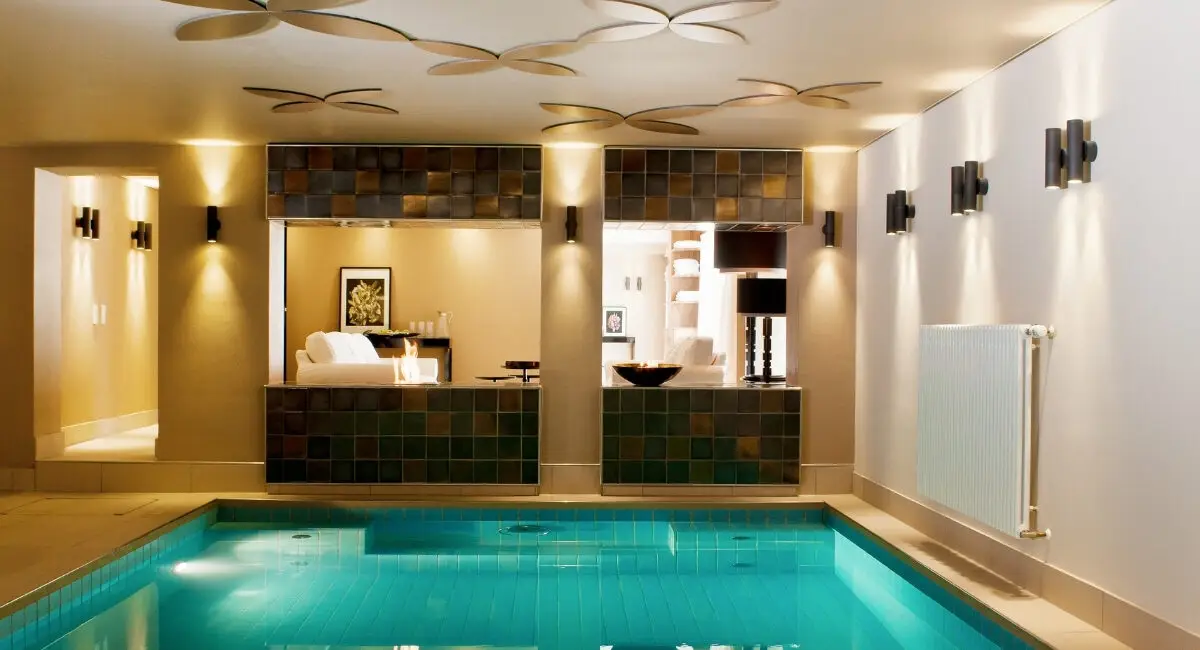 Beleuchtetes Schwimmbecken mit türkisem Wasser und Blütenelementen an der Decke im Taufstein Spa