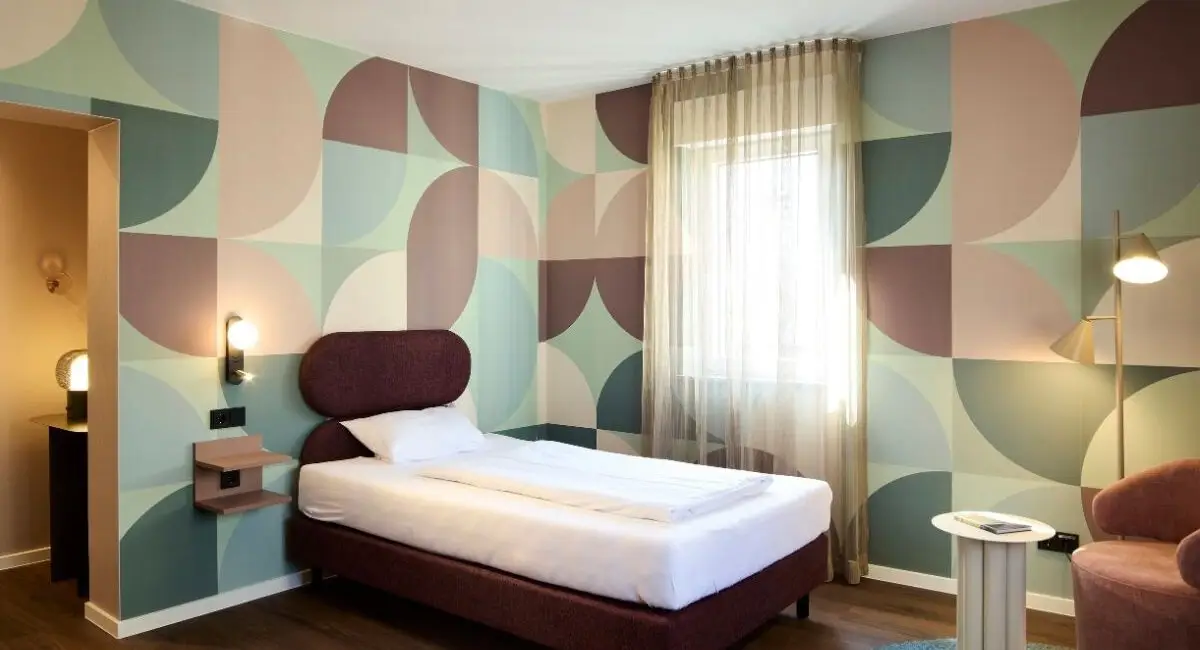 Einzelbett vor rundum geometrisch tapezierten Wänden im Gästehaus 2, Haus der Standesbeamten