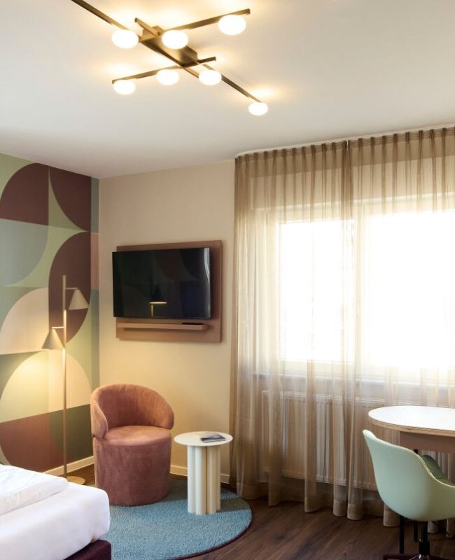 Zimmer mit Schreibtisch, Wandfernseher und Sputnik-Deckenleuchte im Gästehaus 2, Haus der Standesbeamten