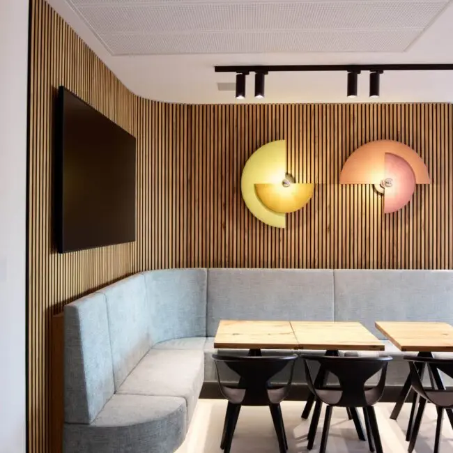 Lounge mit hellblauer Eckbank, Holzlamellenwand und runden Wandleuchten bei Alt & Partner