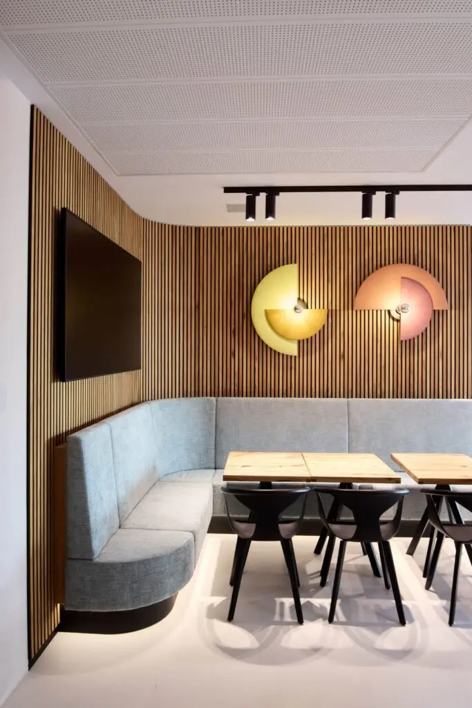 Lounge mit hellblauer Eckbank, Holzlamellenwand und runden Wandleuchten bei Alt & Partner