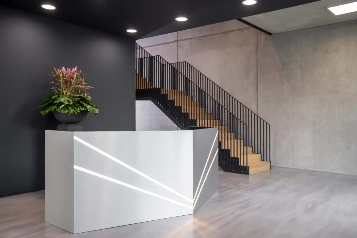 Empfangstresen mit Lichtlinien vor dunkler Wand und Stahltreppe bei Belfox