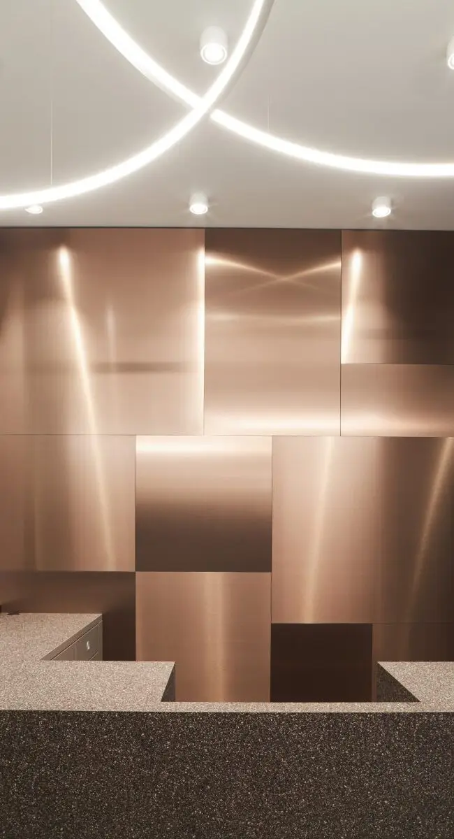 Kupferpaneele hinter Terrazzo-Empfang unter geschwungenen Lichtlinien, Lobby im Haus der Standesbeamten