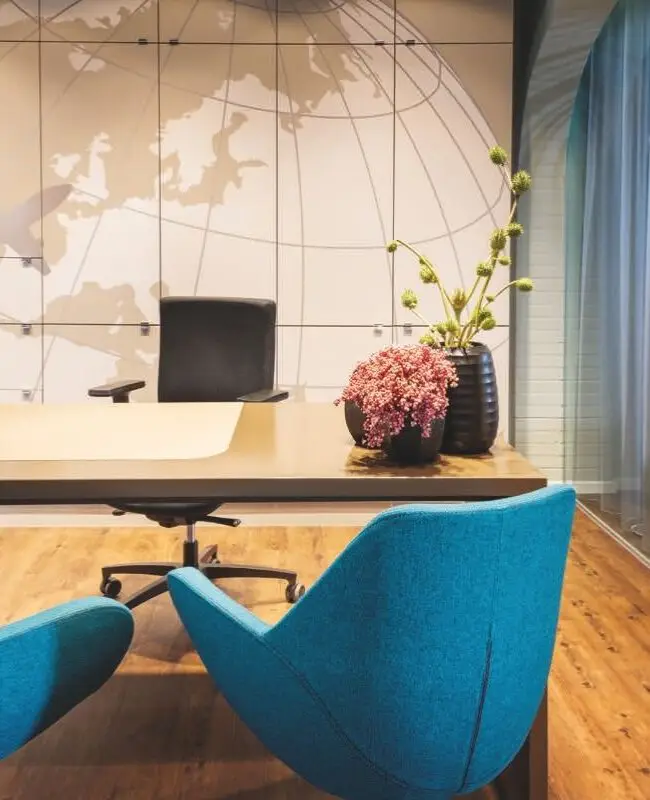 Beratungstisch mit zwei blauen Sesseln vor Weltkarten-Wand bei Merican Reisebüros