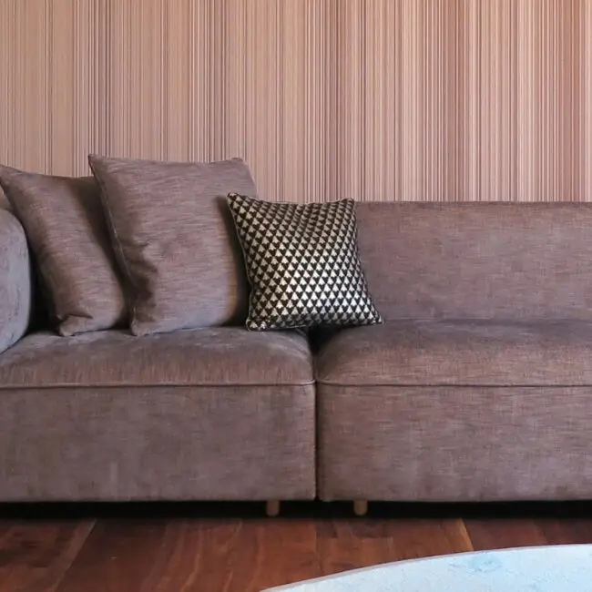 Taupefarbenes Sofa mit Kissen vor feingestreifter Wandtapete im Haus S