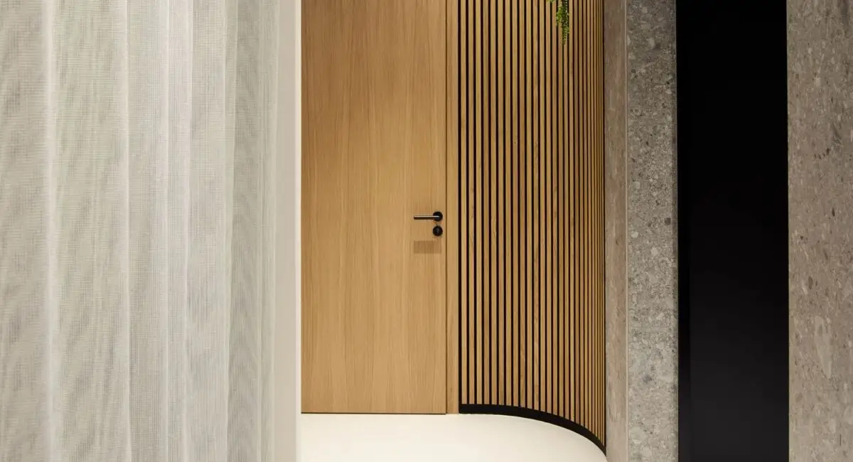 Geschwungener Flur mit Holztür, Lamellenwand und Pflanzen unter Lichtband bei Alt & Partner