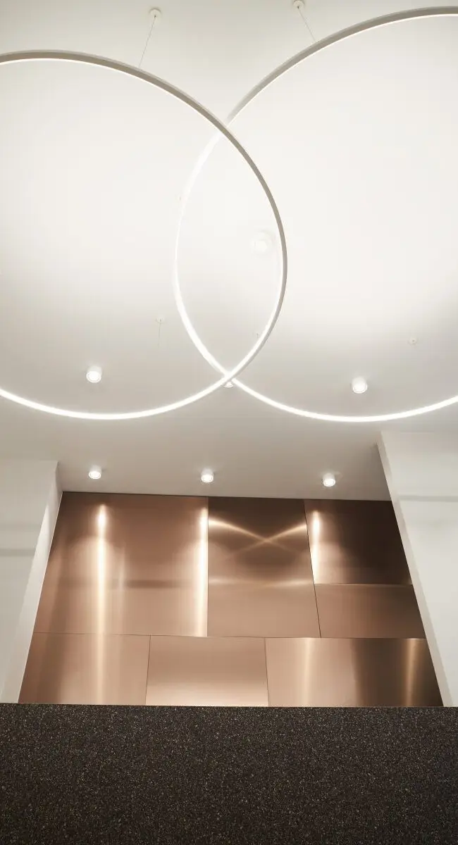 Zwei überlappende Lichtringe über kupferfarbenem Wandbereich, Lobby im Haus der Standesbeamten