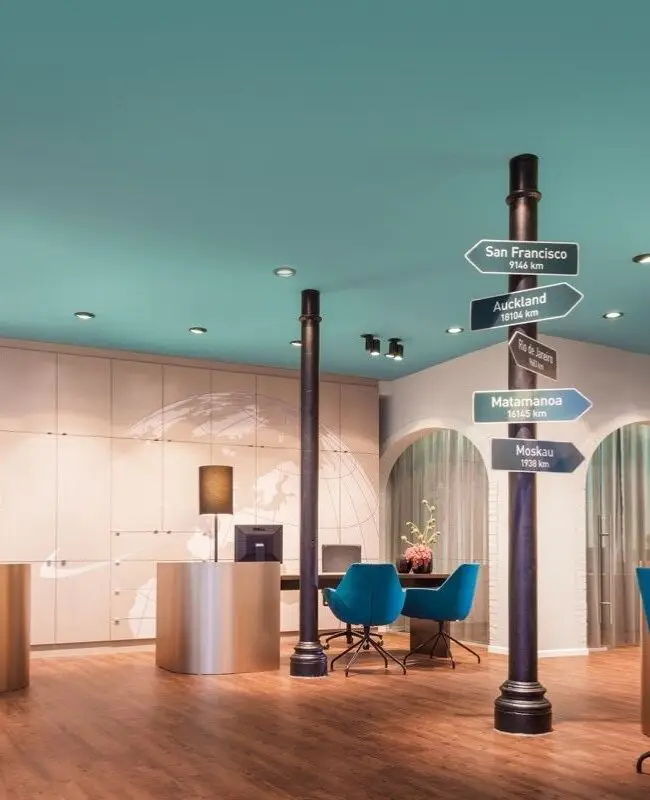 Reisebüro mit petrolfarbener Decke, Wegweiser-Säule und blauen Sesseln bei Merican Reisebüros
