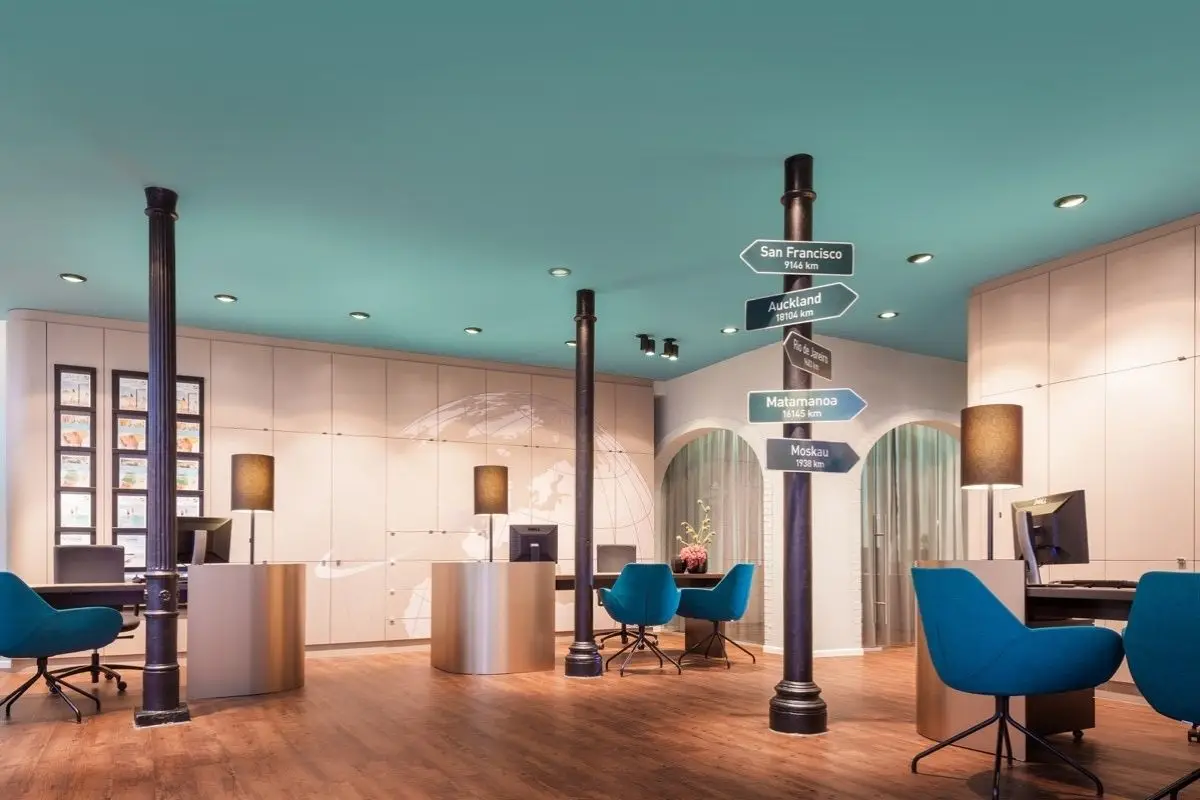 Reisebüro mit petrolfarbener Decke, Wegweiser-Säule und blauen Sesseln bei Merican Reisebüros