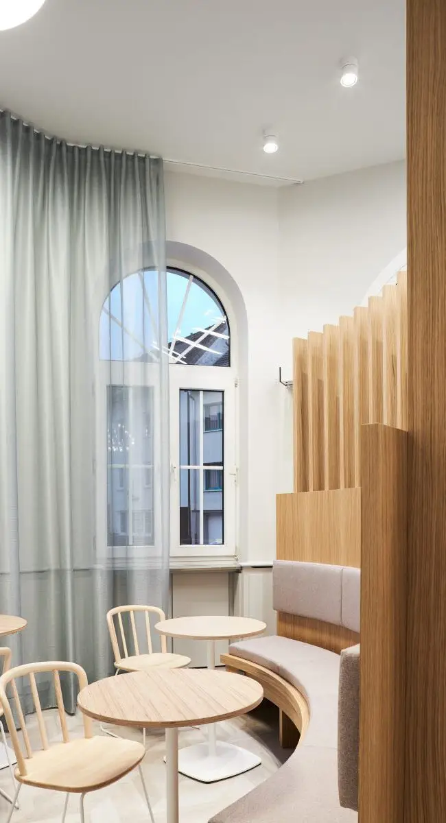 Sitzecke mit Holzstühlen am Rundbogenfenster mit grauem Vorhang, Lobby im Haus der Standesbeamten