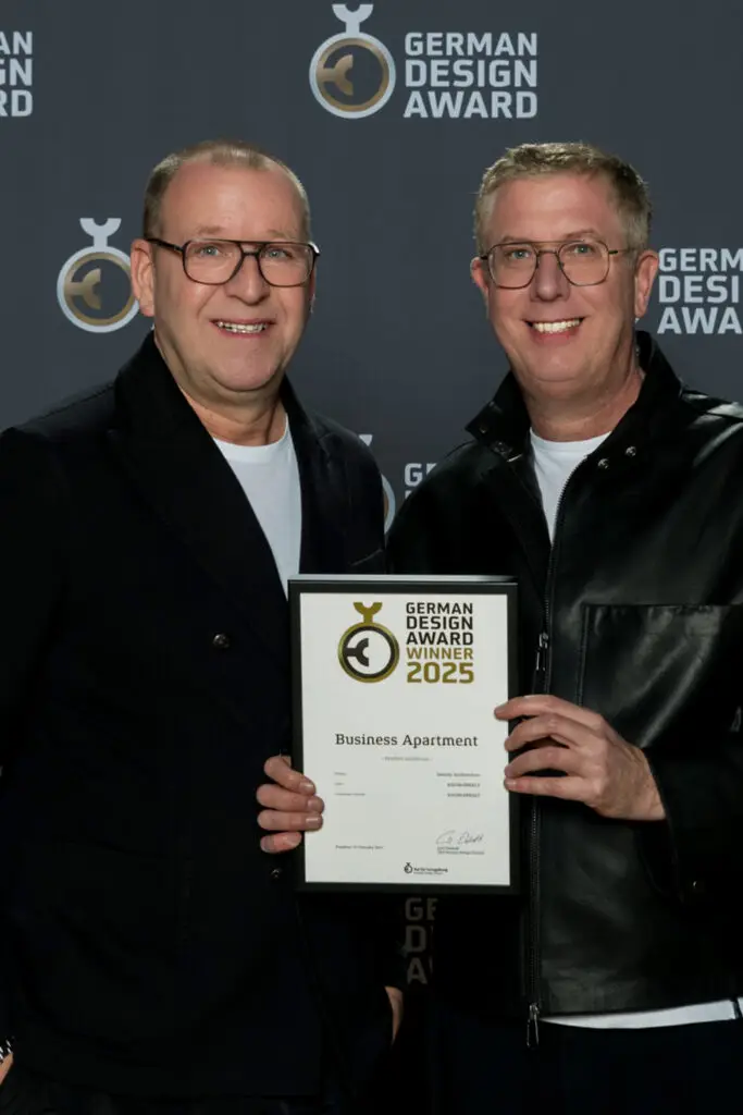 Verleihung German Design Award 2025: zwei Personen von RAUM+INHALT mit der Urkunde „Business Apartment“